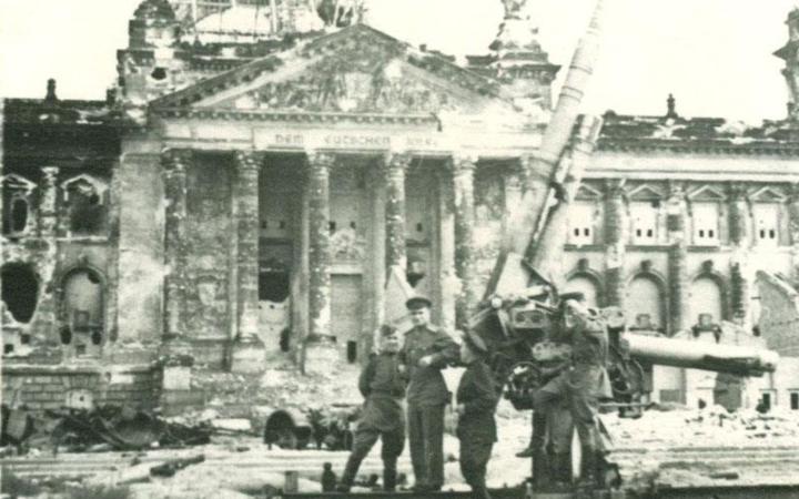 Группа военнослужащих позирует возле разбитого немецкого орудия на фоне поверженного Рейхстага.